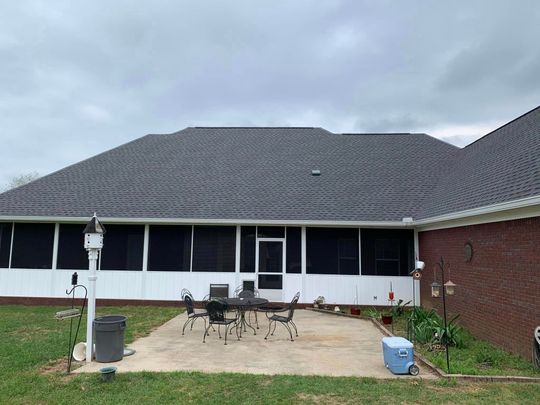 Patio with screened-in porch, dark roof, brick wall, and cloudy sky.