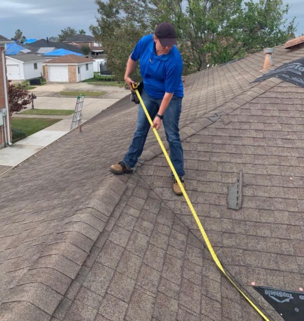 Person in blue shirt measures roof with yellow tape measure.
