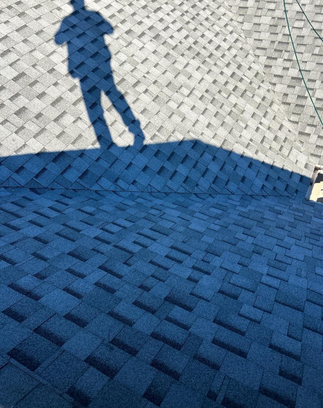 Shadow of a person on a blue and gray shingle roof.