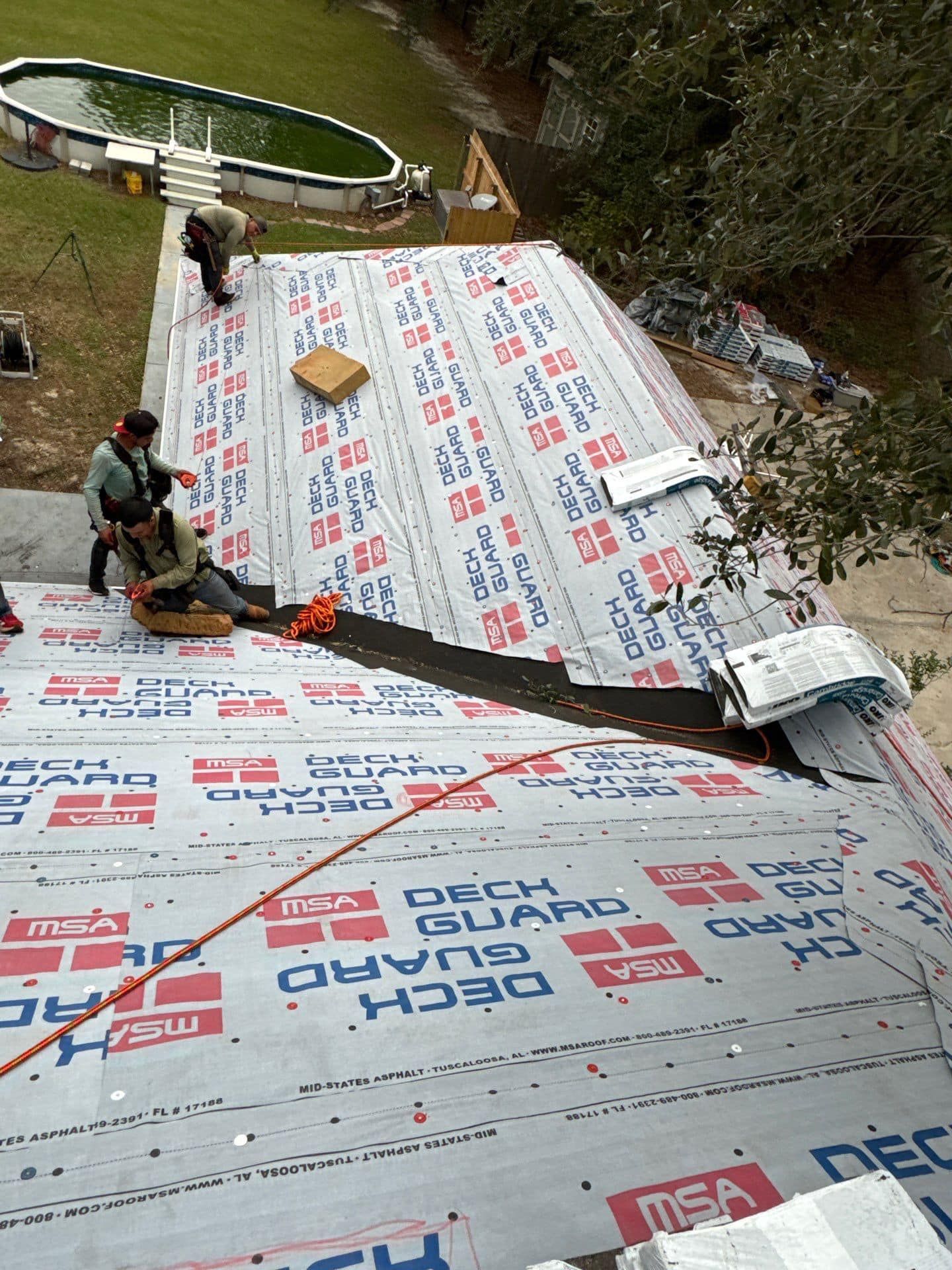 Roofers working on a house roof, installing roofing material. Pool in background. Roofers working on a house roof, installing roofing material. Pool in background.