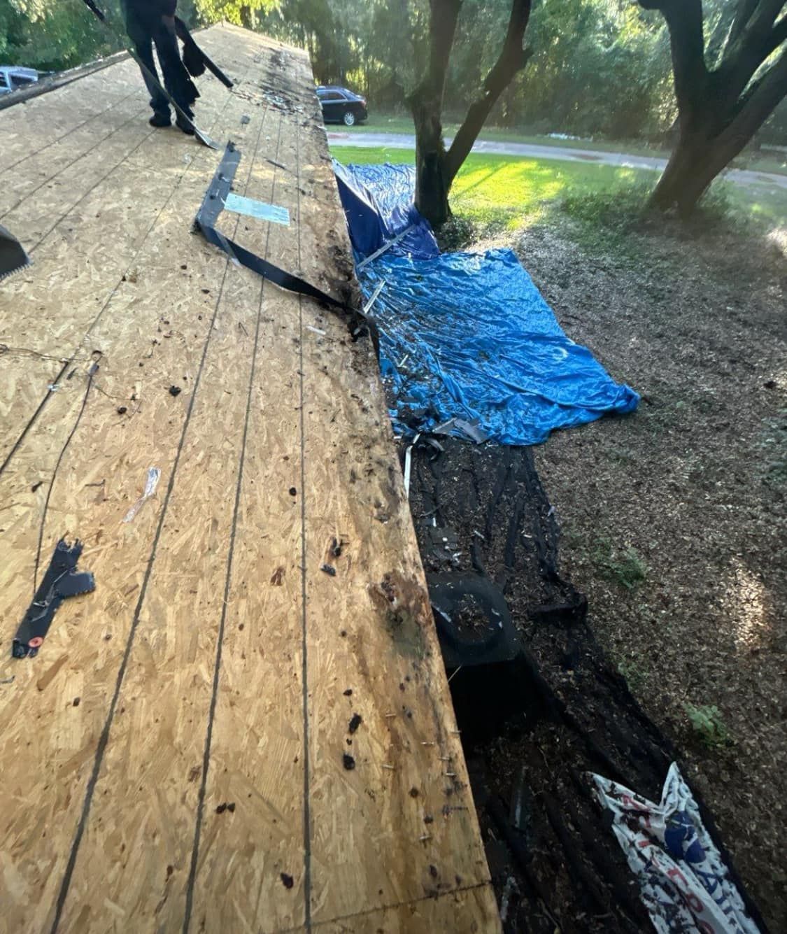 Roof being repaired with exposed wood, blue tarp, and debris.