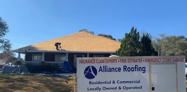 A house with new roofing; a sign for Alliance Roofing in front. Blue sky.