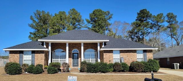 Brick house with dark roof and landscaping against a blue sky.