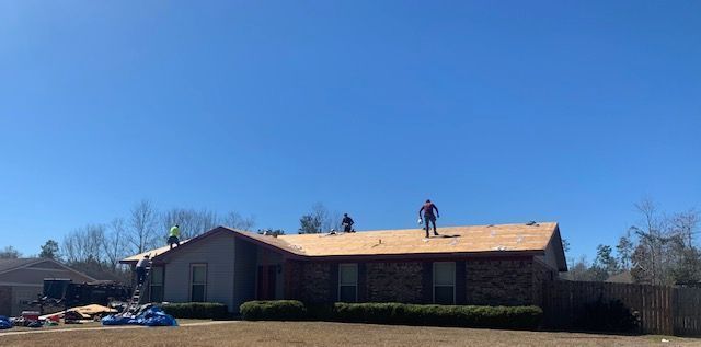 Workers on a roof during a sunny day, likely repairing or replacing it. House is visible below.