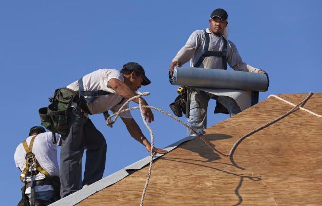 Roofers working on a roof, installing materials. Blue sky in background.