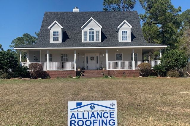 House with a newly installed dark gray shingle roof, white trim, and a sign for Alliance Roofing.