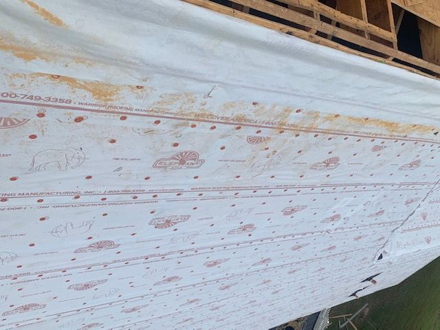 White building wrap with red print partially covers wooden structure, showing staples and construction details.