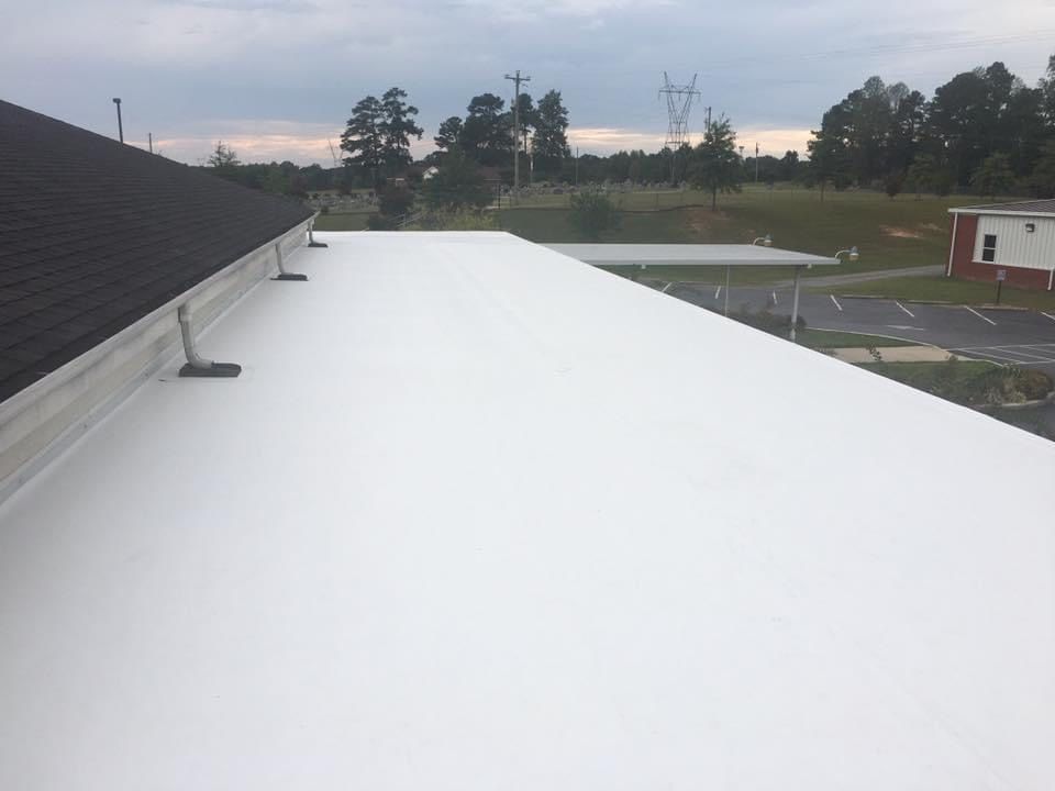 White flat roof next to a dark-shingled roof, with trees and a building in the background.