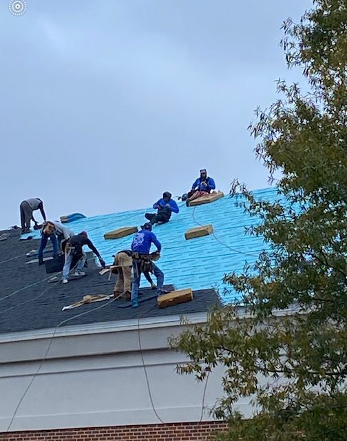 Roofers installing shingles on a roof under a cloudy sky.