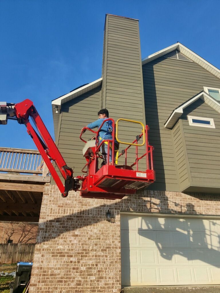 Person in a cherry picker working on a chimney attached to a house with a blue sky.