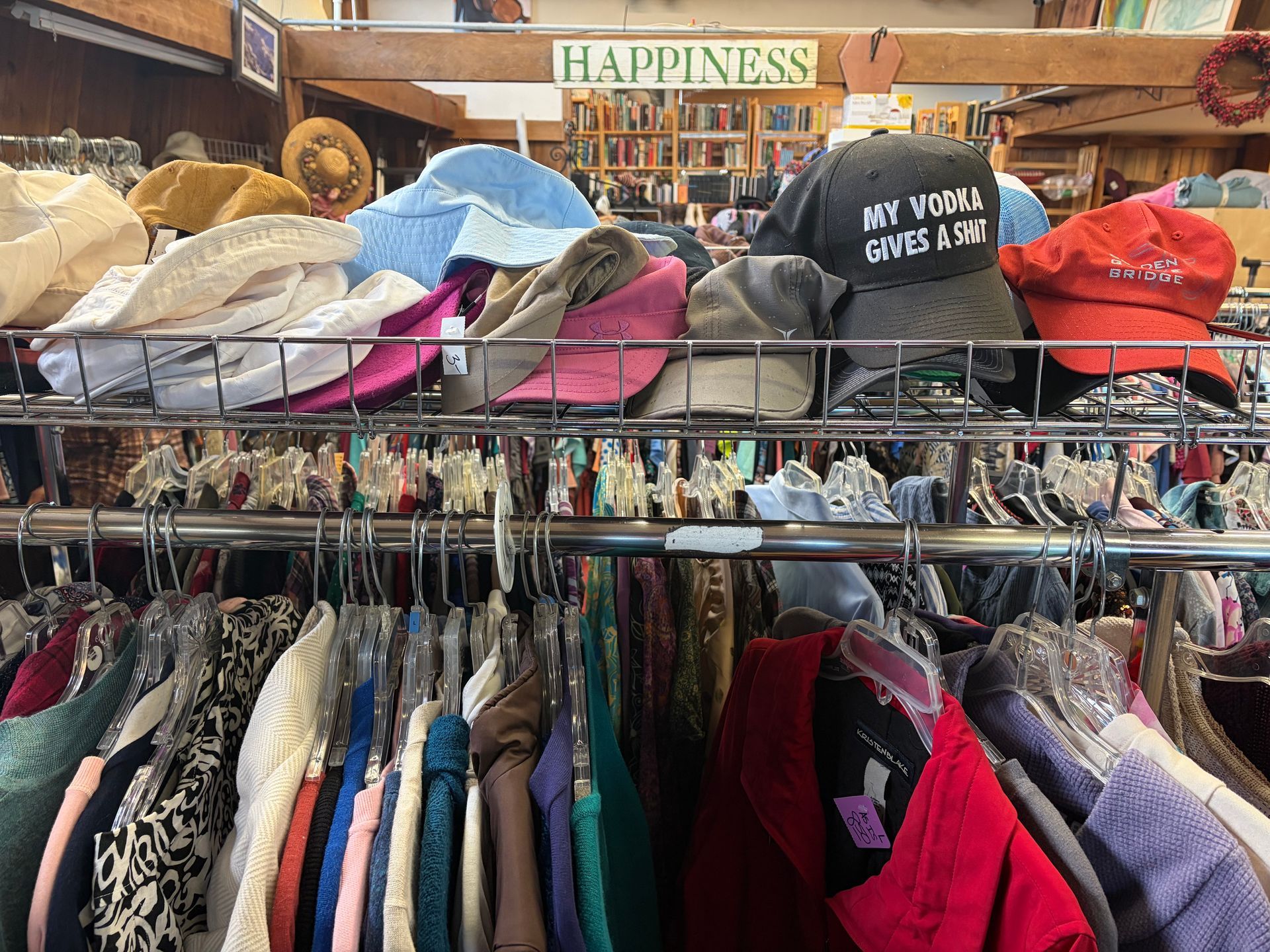Clothes rack in a thrift store, hats on top. Sign says 