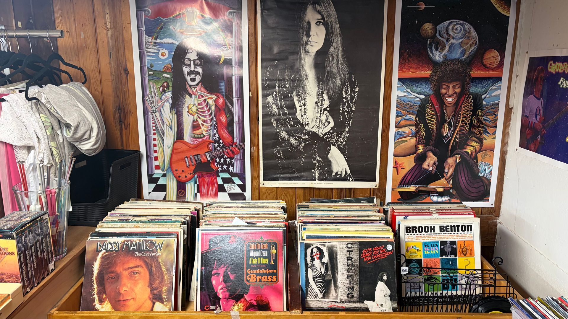 Record store interior with album bins and vintage rock posters: Zappa, Janis Joplin, and others.