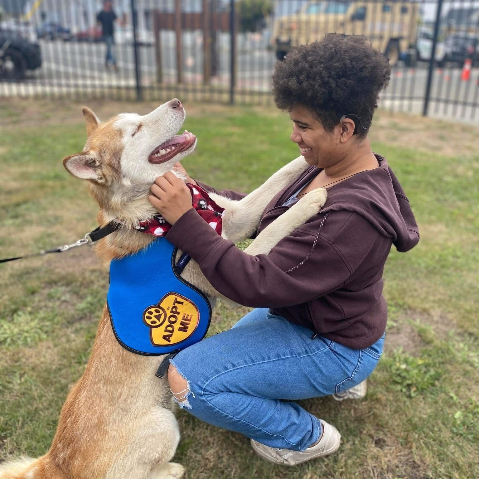 Woman kneeling, hugging a dog wearing an 