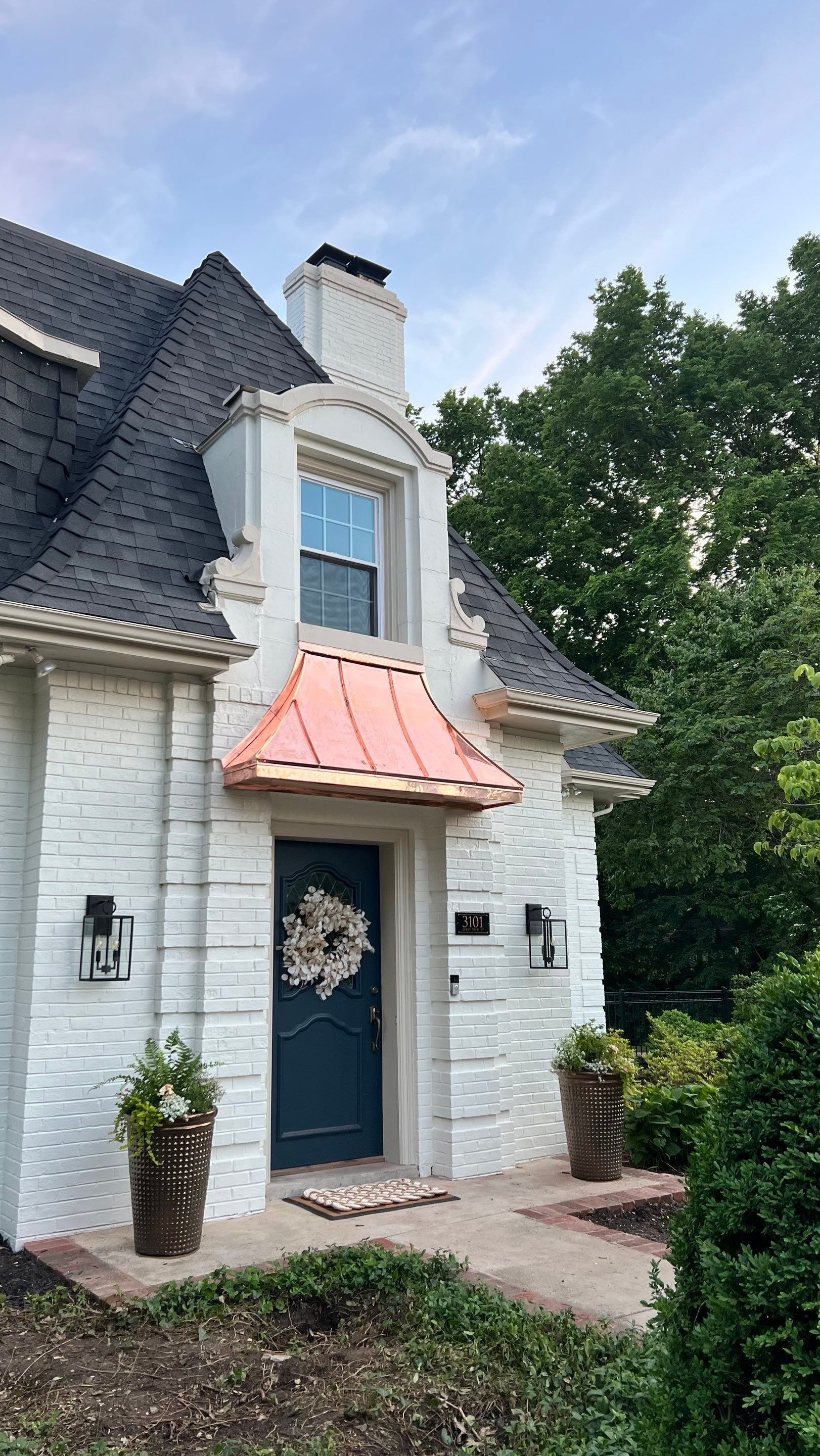 White brick house with a blue door, copper awning, and a black roof.