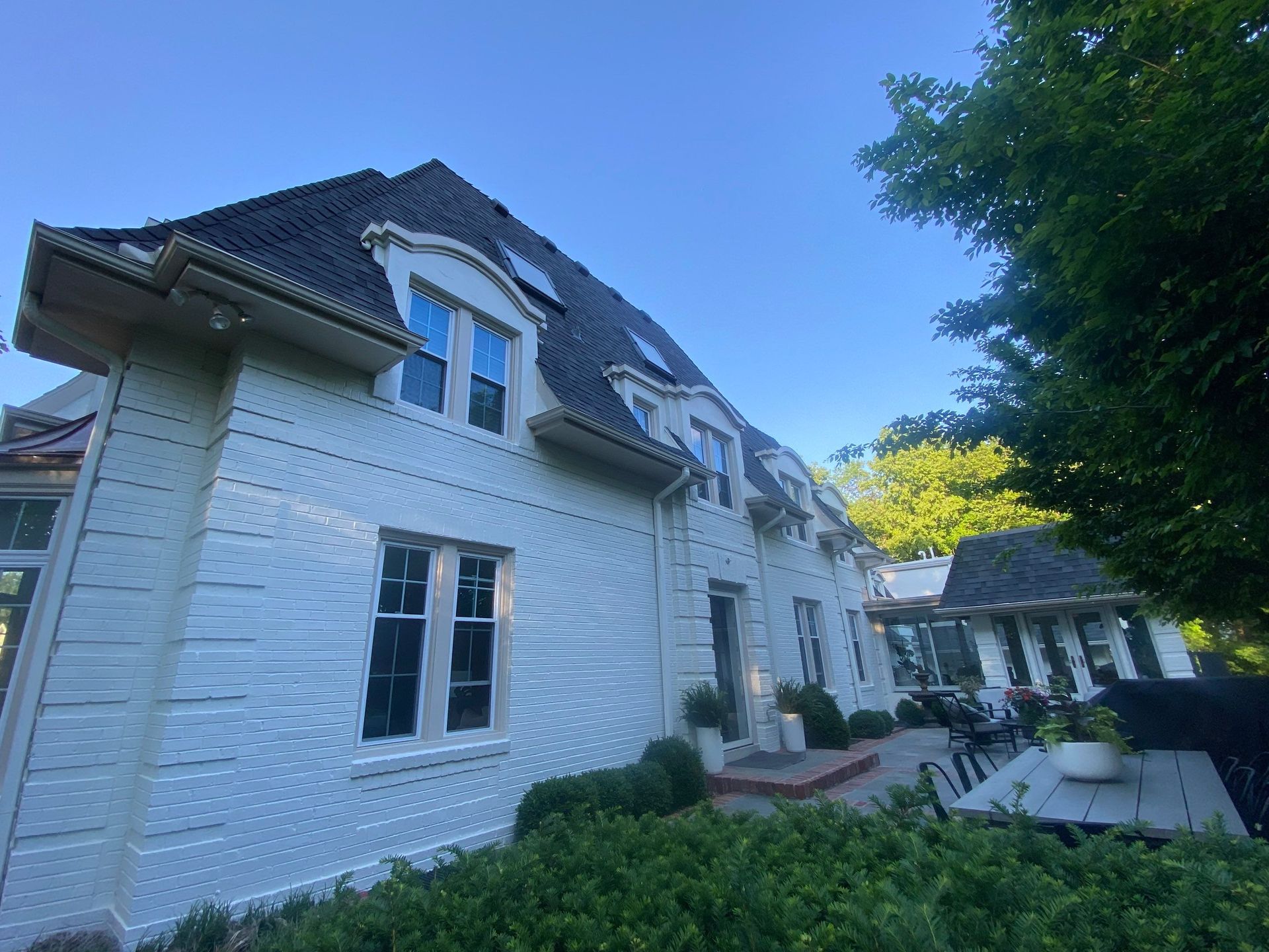 White brick house with dark roof and multiple windows, blue sky.