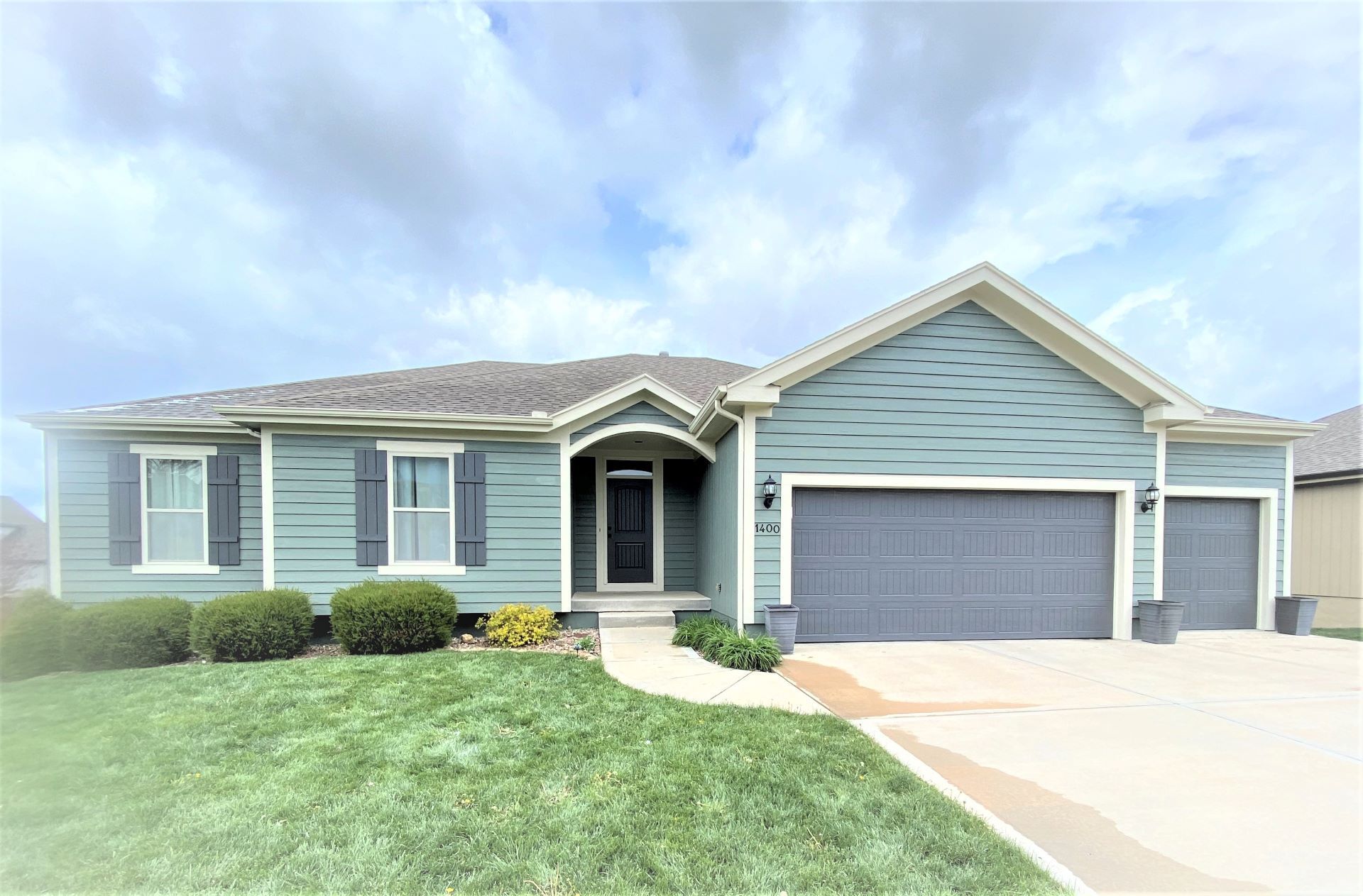 A single-story teal house with gray shutters and a garage on a sunny day.