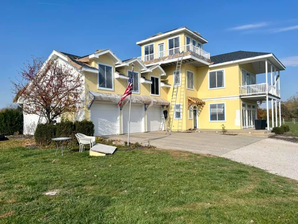 Yellow house with roof construction, American flag, green grass, clear sky.