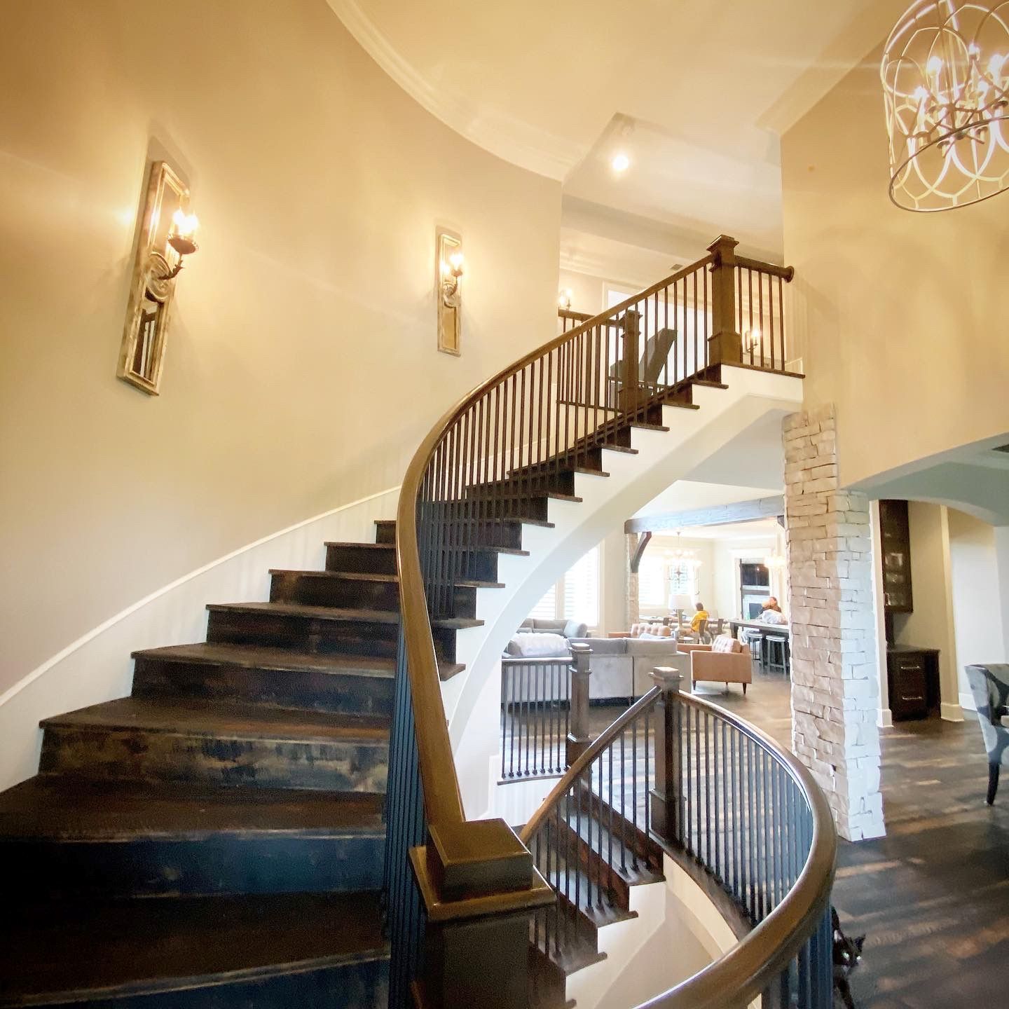 Curving wooden staircase in a home's entryway. Dark wood steps, dark railing, light walls, and chandelier.