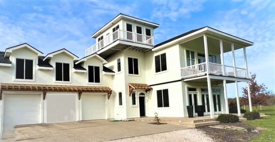 Large, two-story white house with a tower and balcony, set against a blue sky.
