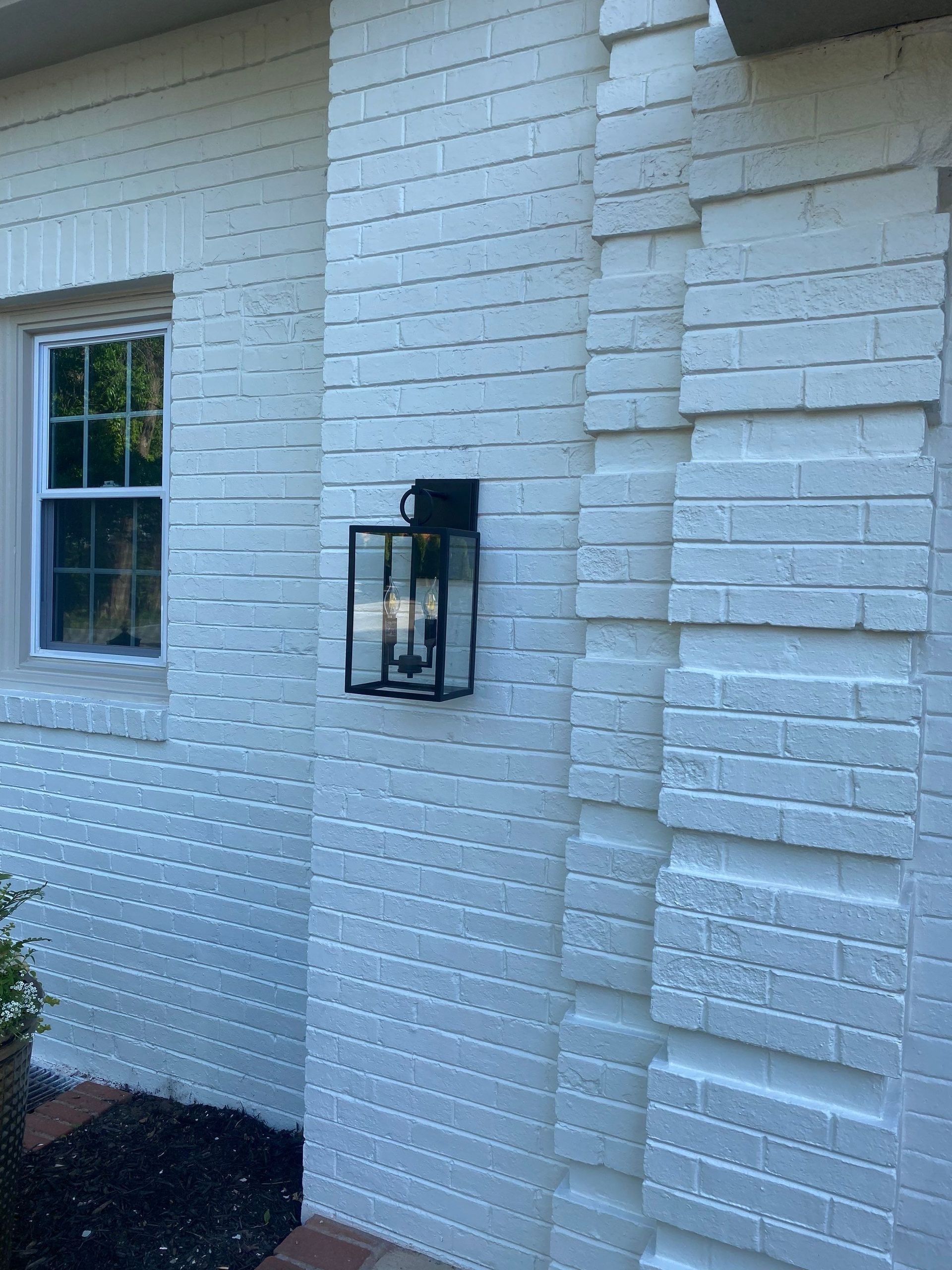 White brick building with a black outdoor light fixture. Window visible.