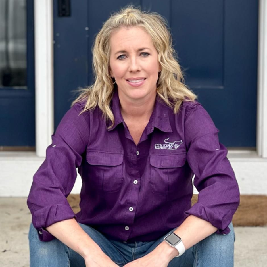 Man on stepladder installing black shutter on gray building wall.