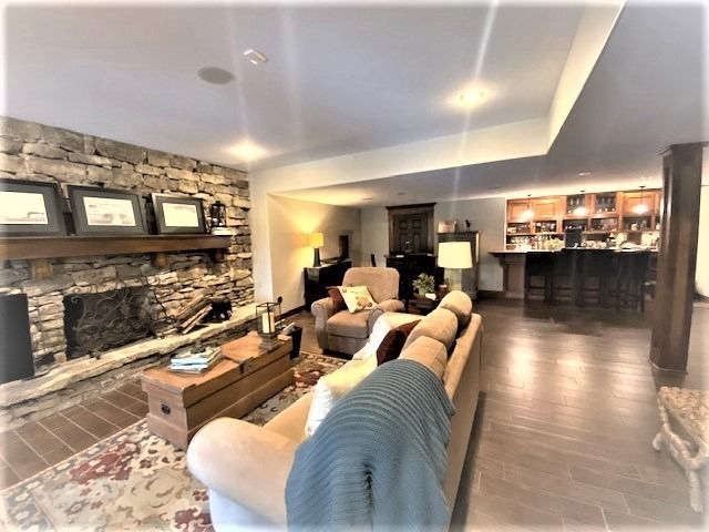 Living room with stone fireplace, bar, and seating area. Wooden floor, beige walls, and soft lighting.