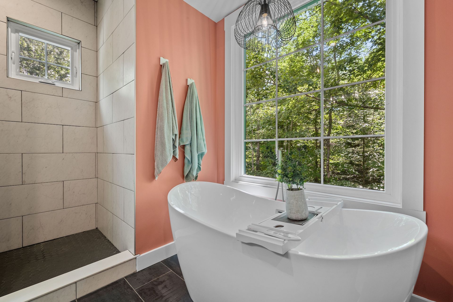 Bathroom with freestanding white tub, shower, and window with view of trees; coral walls.