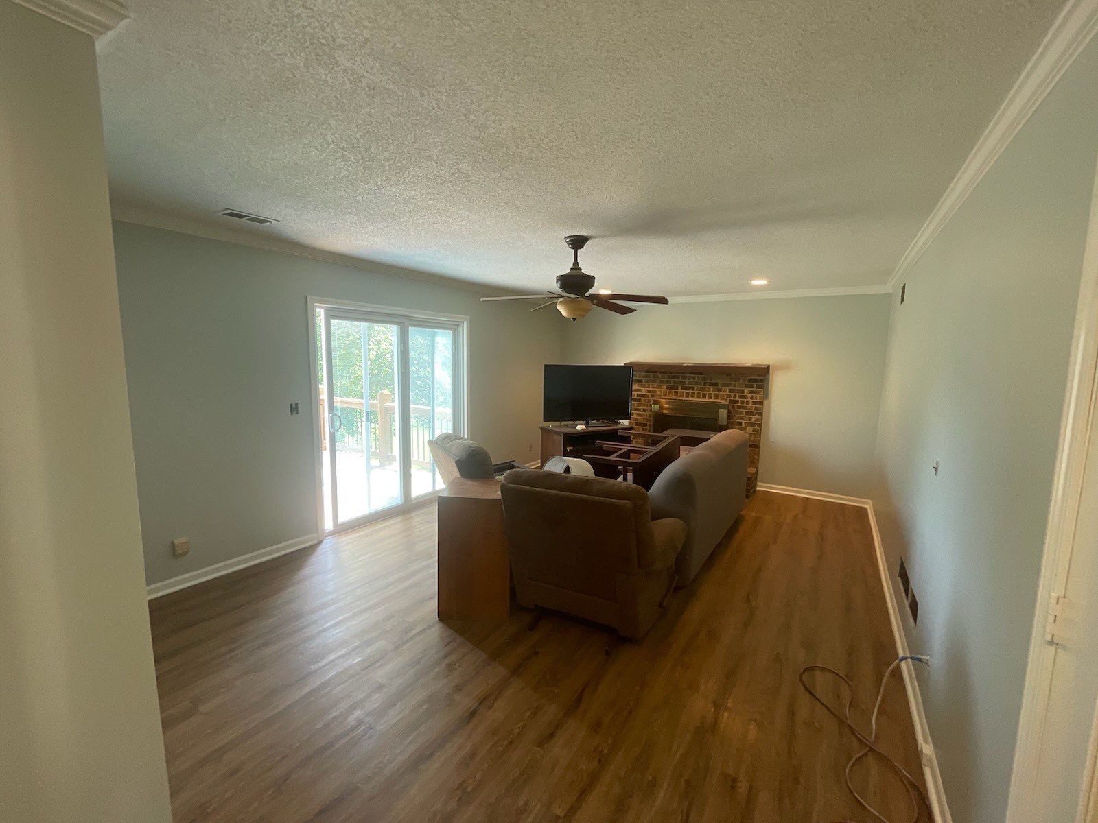 Living room with wood floors, blue-green walls, sliding door, fireplace, television, and ceiling fan.