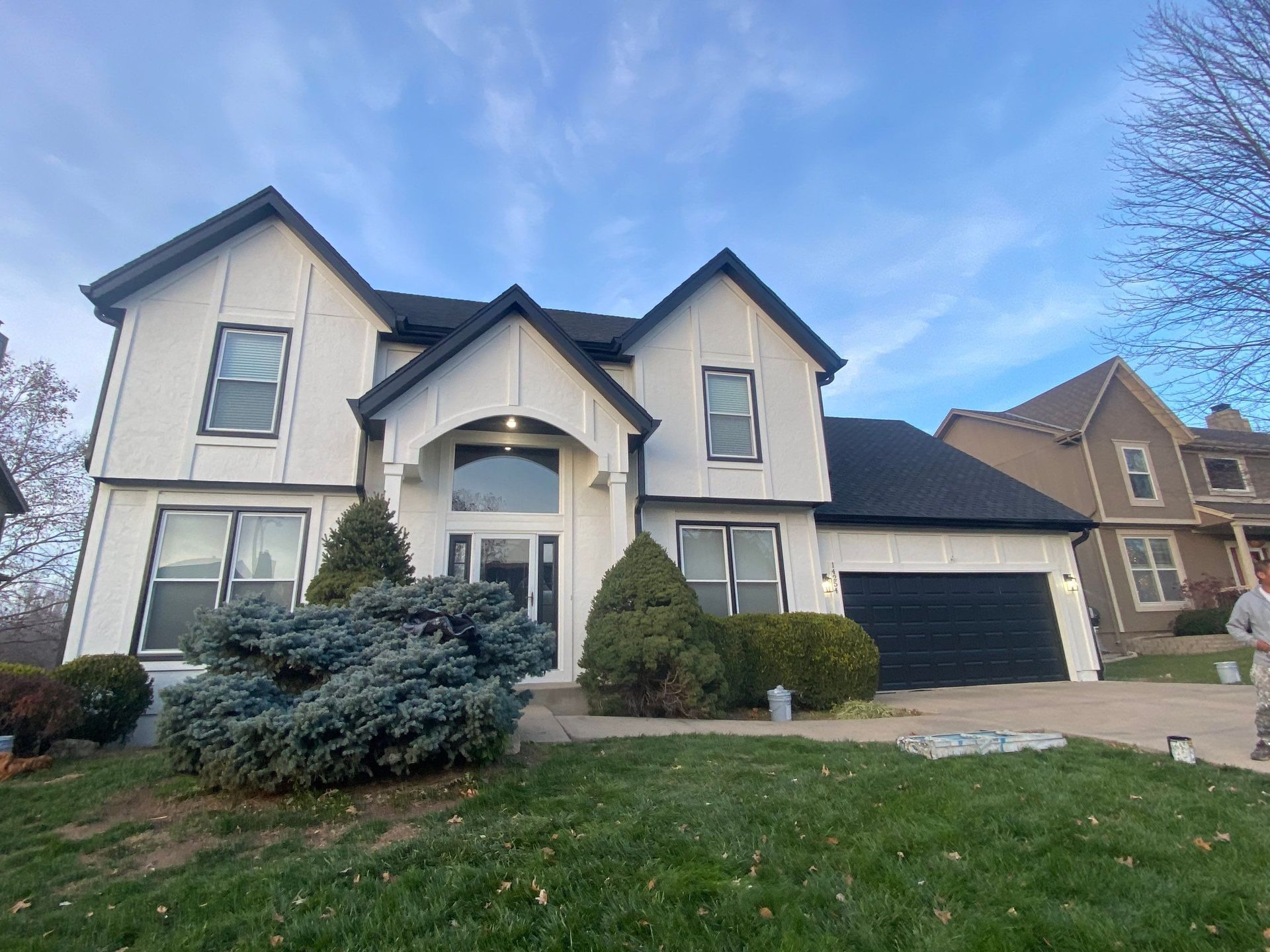 White house with black trim, a black garage door, and a green lawn under a blue sky.