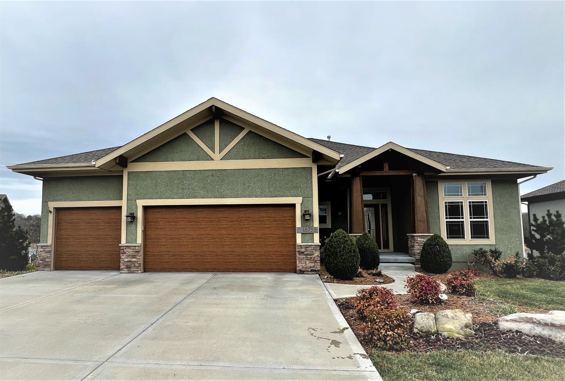 Ranch-style house with green stucco exterior, brown garage doors, and a stone-covered entrance.