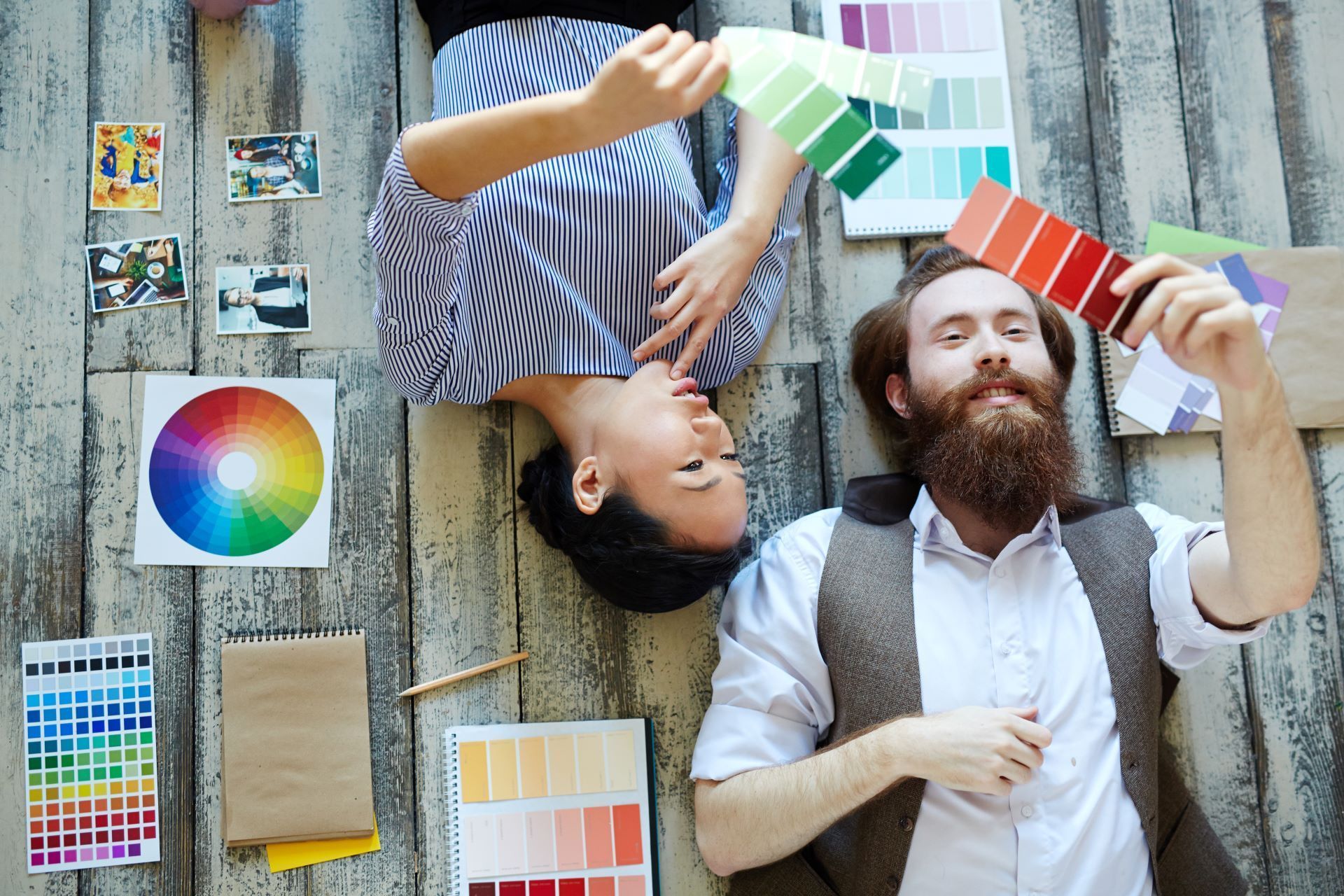 People looking at color swatches, lying on wooden floor with color wheel and design examples.