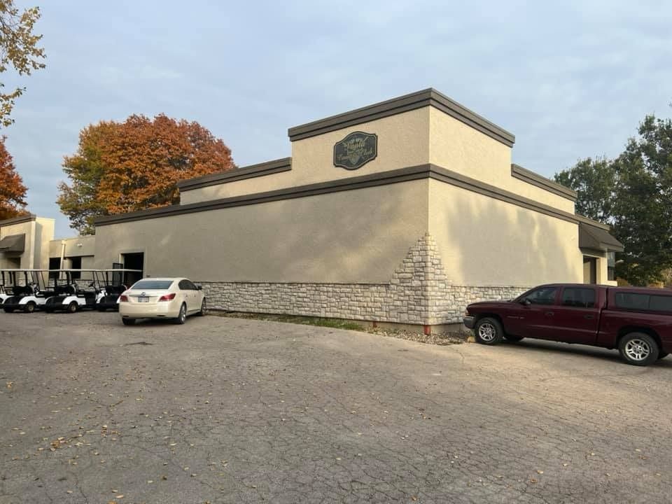Building with beige stucco and stone base, parked cars, and golf carts on a paved surface.