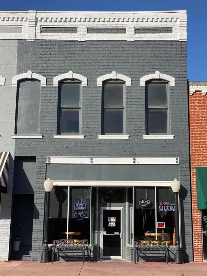 Gray brick building with three windows, a glass storefront, and benches.