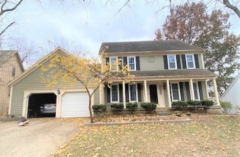 Two-story house with green siding, a two-car garage, and a front porch. Fall foliage visible.