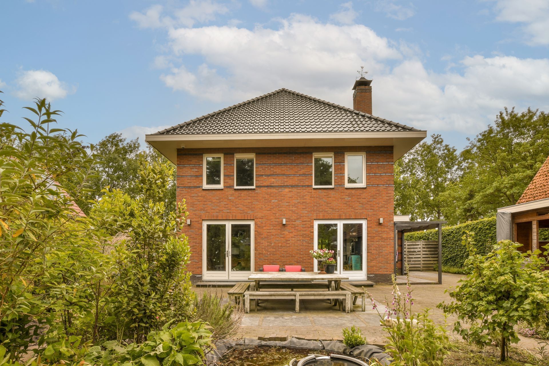 Red brick house with a dark tiled roof, patio, and garden.