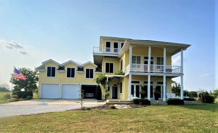 Yellow two-story house with garage, balconies, and American flag on a sunny day.