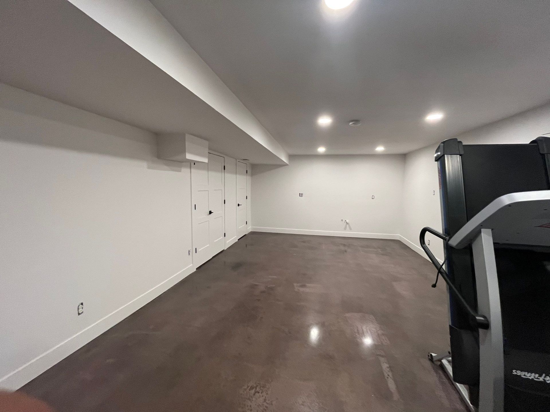 A home gym with a treadmill, hardwood floor, and white walls.