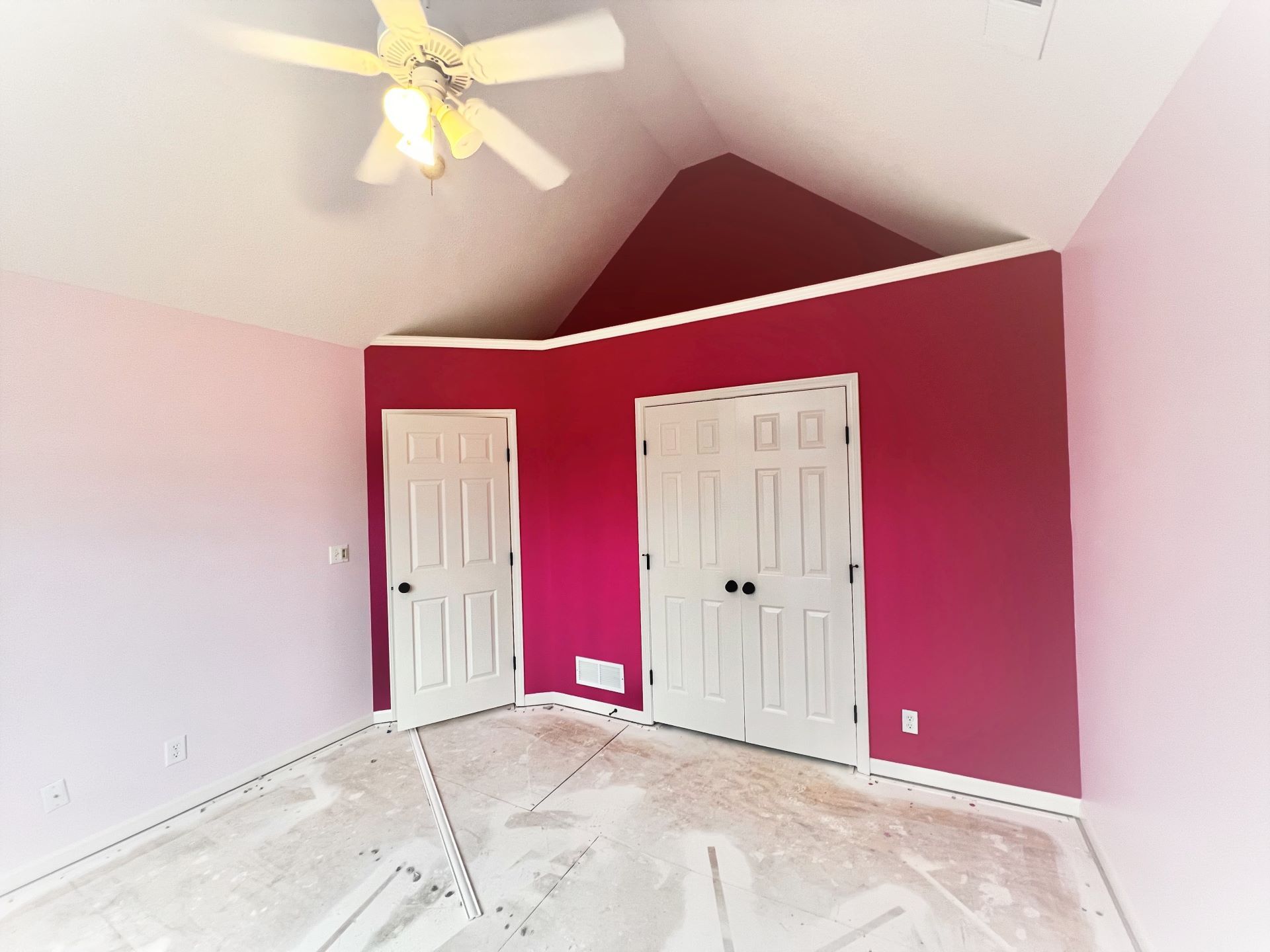 Pink bedroom with white trim, two white doors, and a burgundy accent wall; ceiling fan.