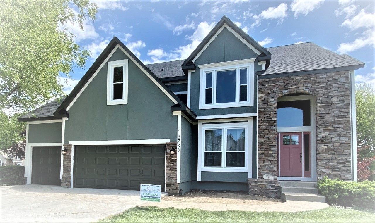 Two-story house with green siding, stone accents, and red front door against a blue sky.