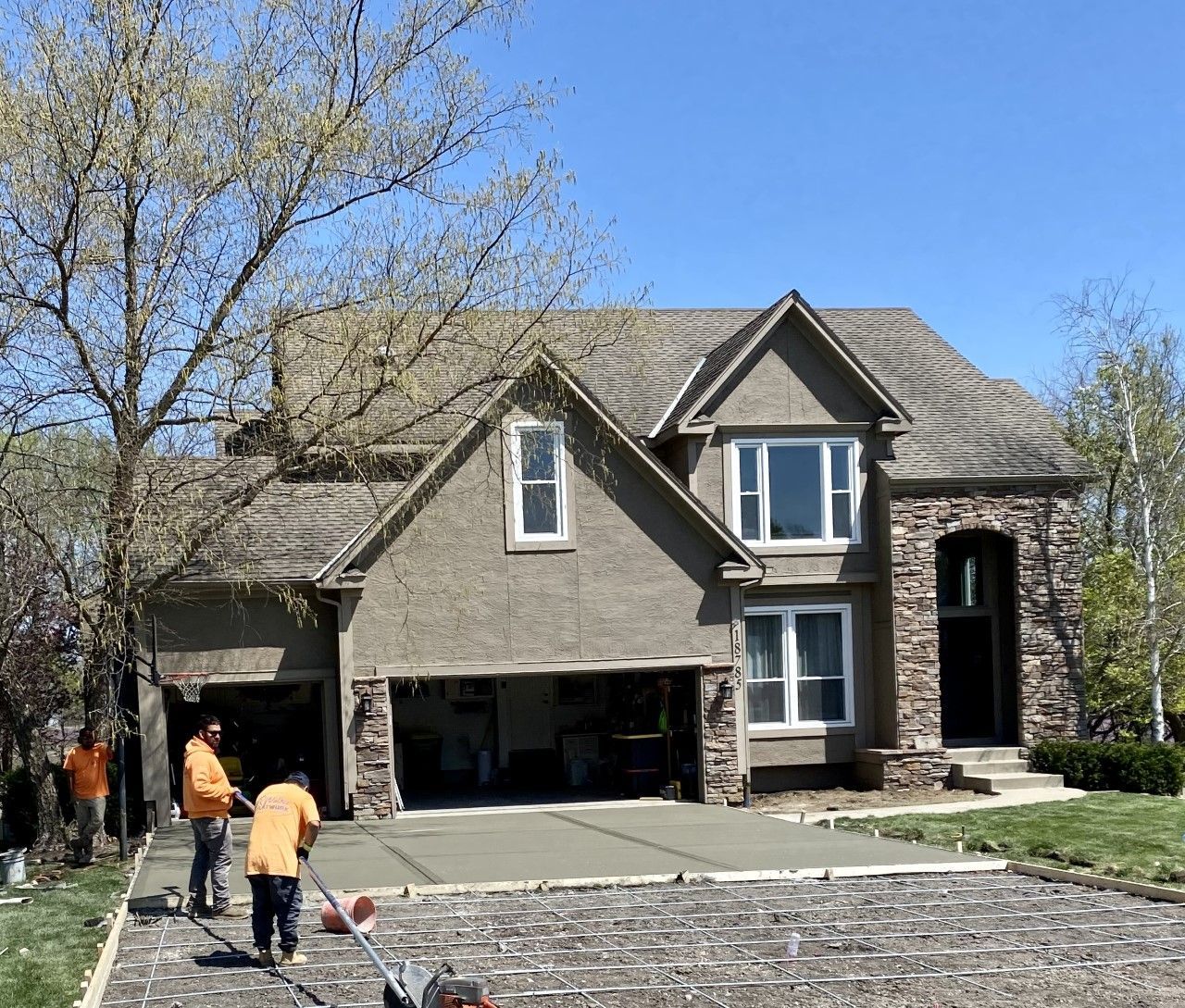 Workers paving a driveway in front of a two-story house with a garage.
