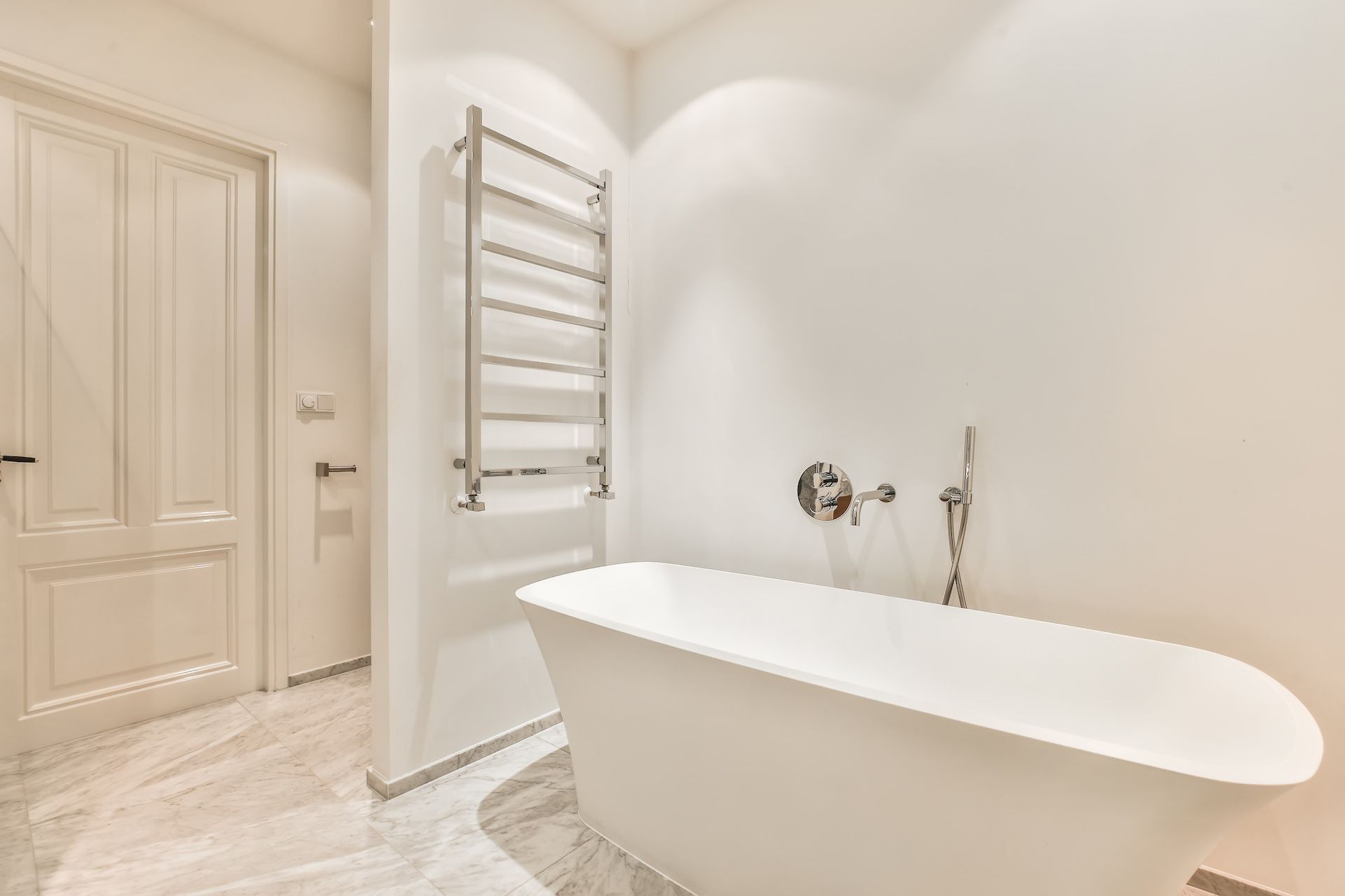 Bathroom with a white freestanding tub, silver towel warmer, and white door.