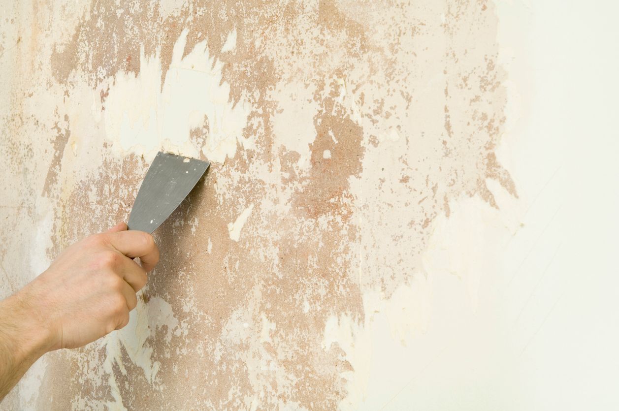 Hand scraping old wallpaper from a wall.