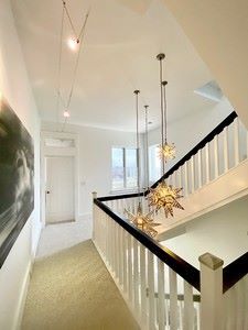 Hallway with starburst pendant lights, white walls, black handrail, stairs, and artwork.