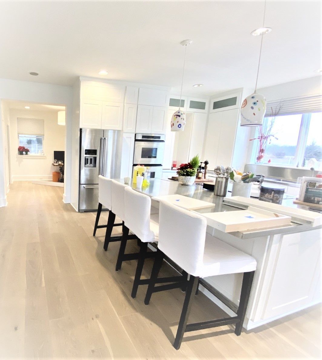 White kitchen with island, seating, and stainless steel appliances. Bright, airy, and modern.