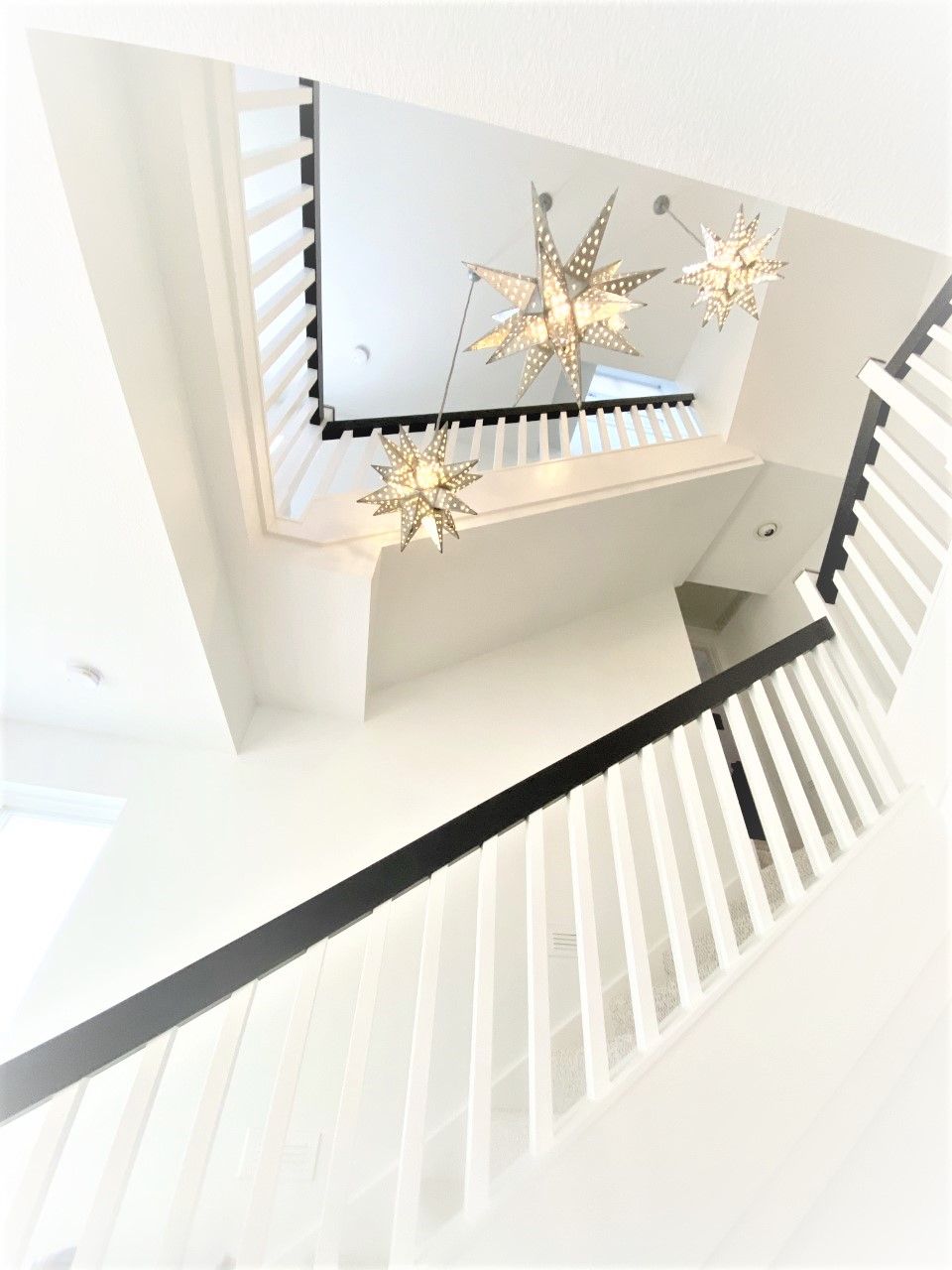 Staircase viewed from below, white walls, black handrail, star-shaped chandeliers.