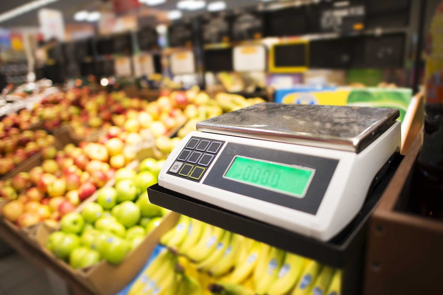 Hay una balanza frente a un expositor de frutas y verduras en una tienda de comestibles.