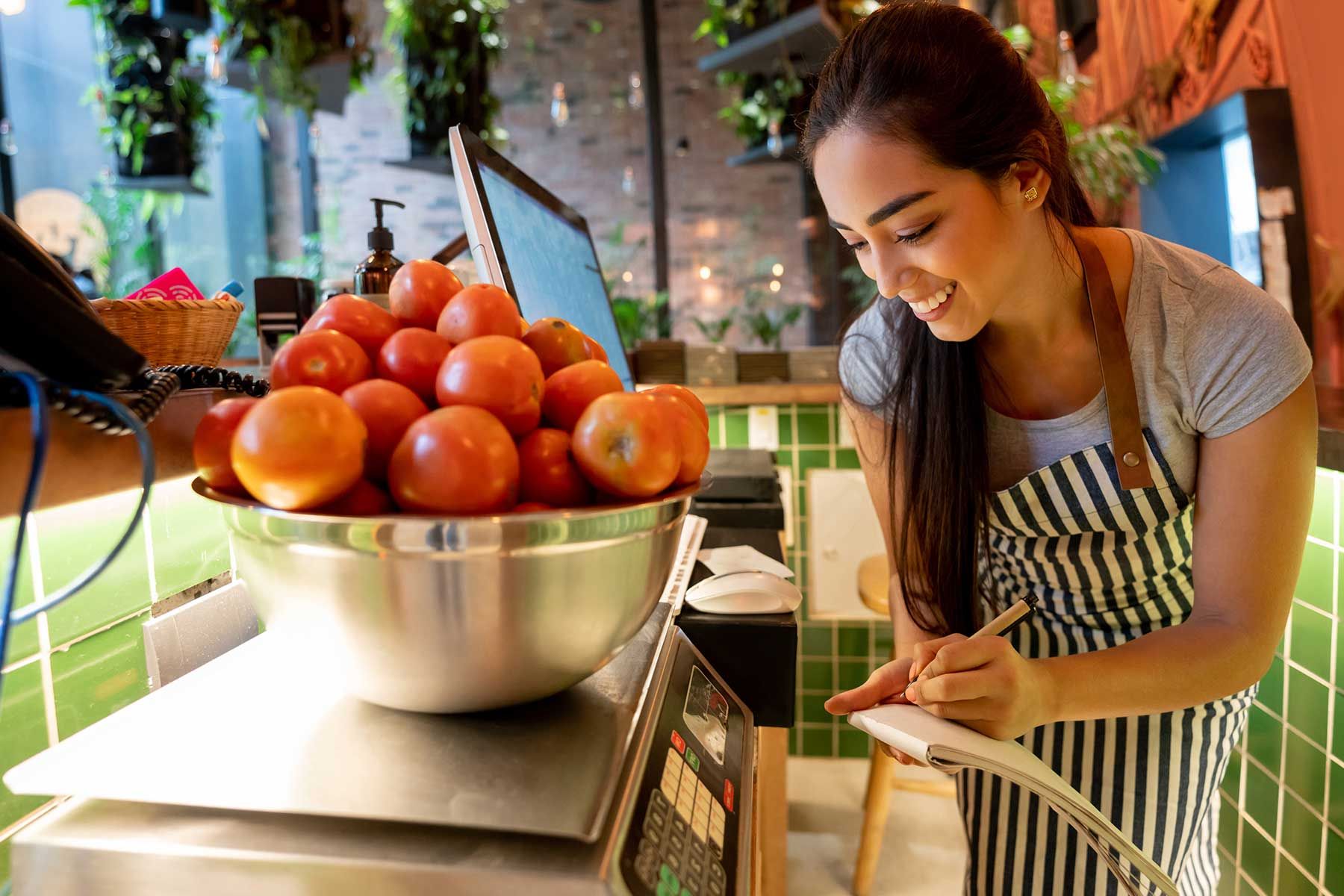 Una mujer está parada frente a un plato de manzanas en una balanza.