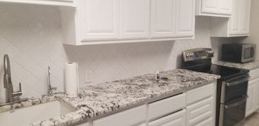 A kitchen with white cabinets , granite counter tops , a stove , sink and microwave.