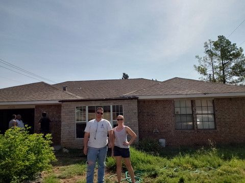 A man and a woman are standing in front of a brick house.