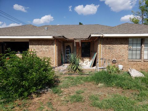 A brick house with a broken roof and a ladder in front of it.